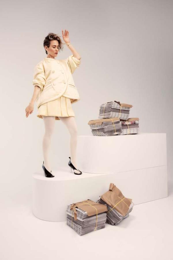Sarah Paulson standing on podium with bundles of New York Posts.