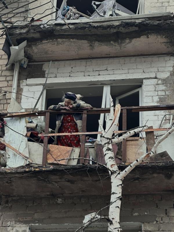 An elderly civilian woman stands with a cat on the balcony of her destroyed house in the city of Avdiivka.