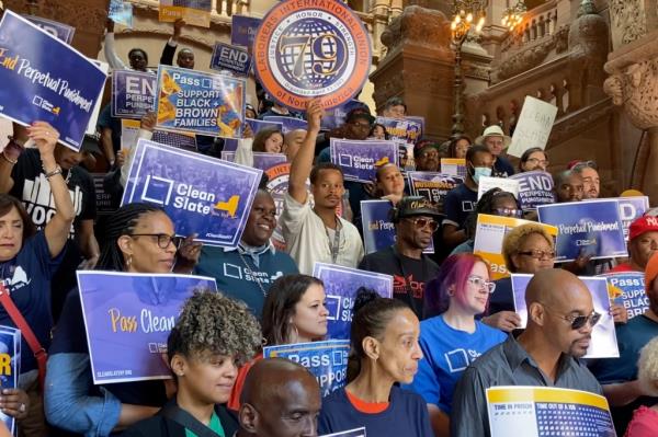 A crowd of people rallying for Clean Slate bill inside the NYS Capitol with some holding unio<em></em>n signs.