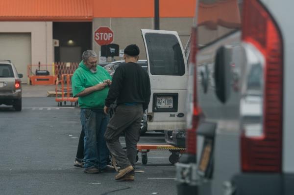 a Home Depot shopper pulls bills out of his wallet to tip a migrant who helped him transfer his purchases into his car