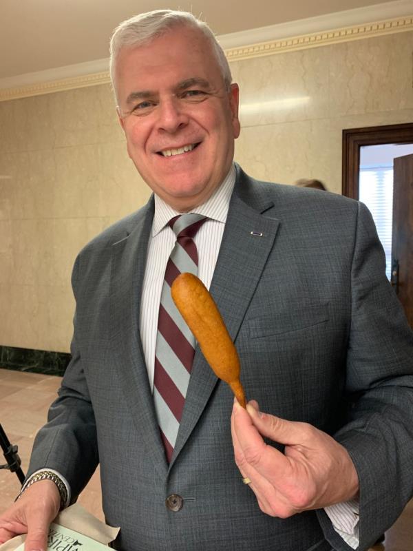 Assemblyman Joe Angelino in a suit holding a corn dog during a late-budget pay freeze
