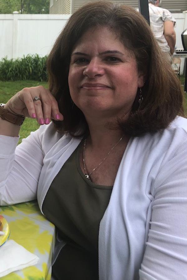 Lois Herrera sitting at a table smiling for camera wearing white sweater and green shirt