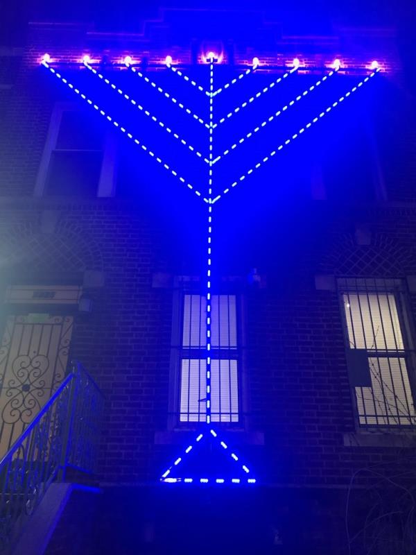 20 foot tall stainless steel menorah with blue lights up against a house