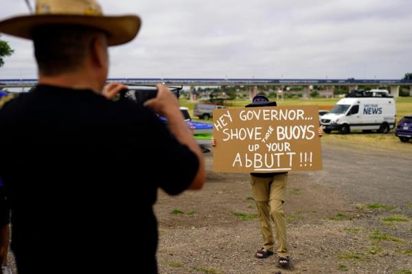 A woman holds a sign in protest of buoys that are set to be deployed in the Rio Grande, Friday, July 7, 2023
