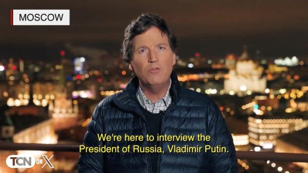 Tucker Carlson speaks to camera in a jacket with a background of people. Supplied image from the Carlson Network's interview with Vladimir Putin in Moscow.
