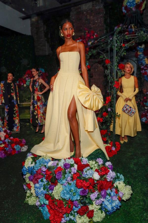 Bad Gyal posing in a pale yellow gown with a flirty thigh-high slit and bow at the alice + olivia by Stacey Bendet Spring 2025 Presentation in New York City.