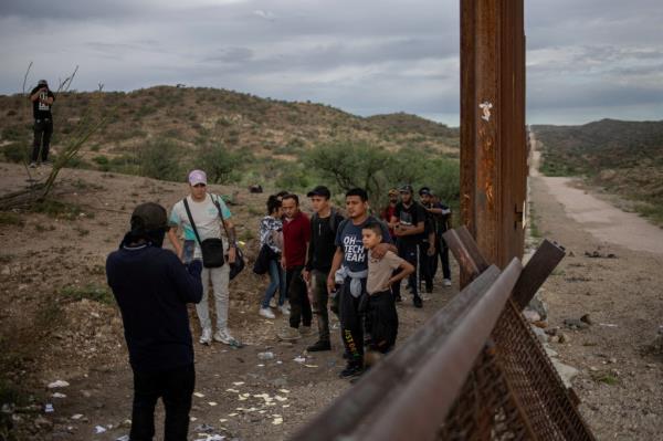 A smuggler covers his face in the background as another photographs migrants before they cross the Border Wall into the United States from Sonora, Mexico as photographed from Ruby, Arizona, U.S., June 26, 2024.