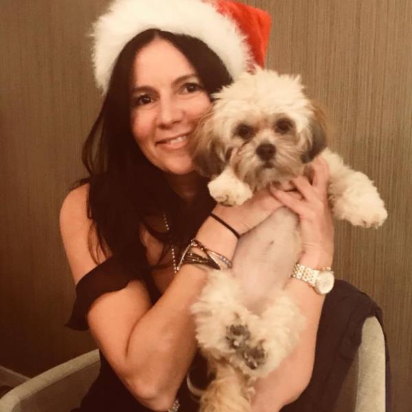 Nadia Vitel, a brunette woman holding a small dog and wearing a santa hat.