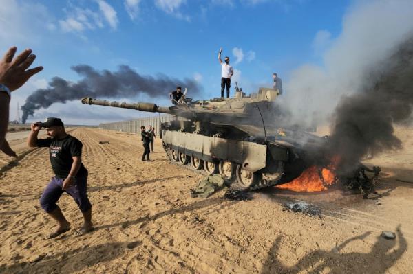 Palestinians celebrate by a destroyed Israeli tank at the Gaza Strip fence east of Khan Younis southern Saturday, Oct. 7, 2023.