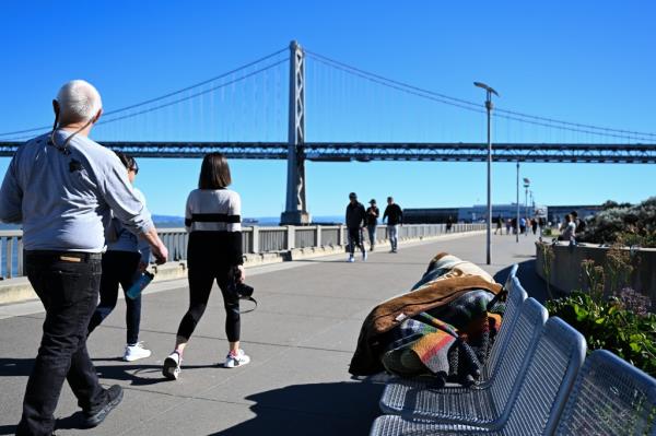 A homeless sleeps on a bench near Ferry Building as daily life co<em></em>ntinues in San Francisco.