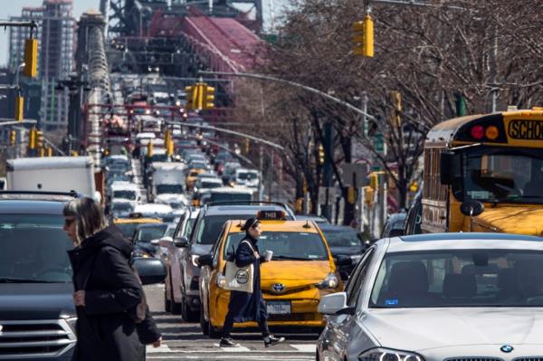 Pedestrians crossing Delancey Street in Manhattan with co<em></em>ngested traffic from the Williamsburg Bridge, featuring Jin Ziwei walking among the crowd
