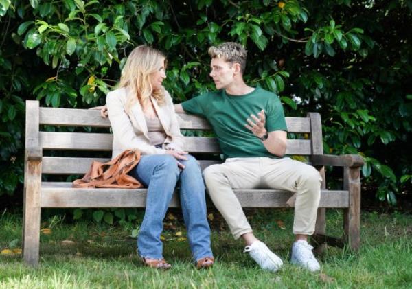 Cindy and Peter sit together on a bench in EastEnders