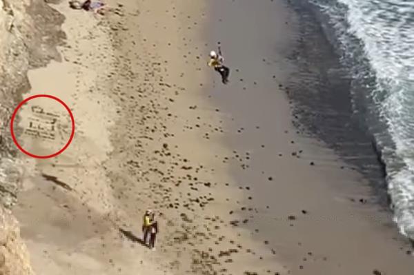 Kite surfer being rescued off a beach, havin<em></em>g spelled out 'HELP' with rocks, spotted by a private helicopter