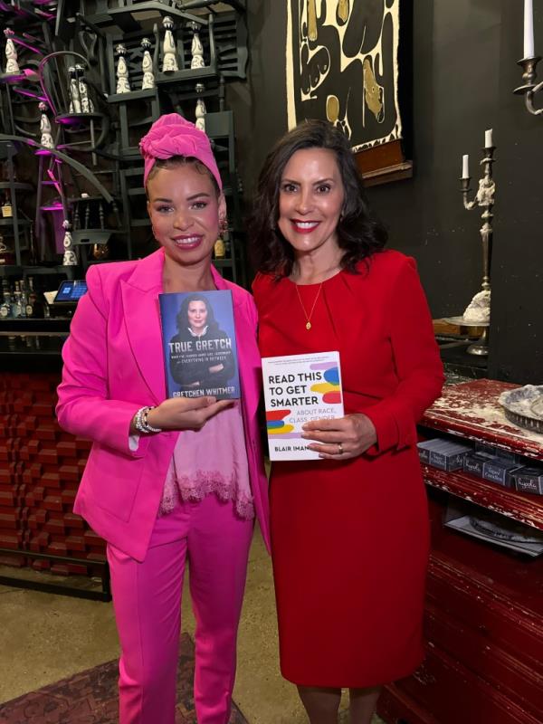 Blair Imani Ali and Mayor Gretchen Whitmer in pink suits, holding a book during an interview