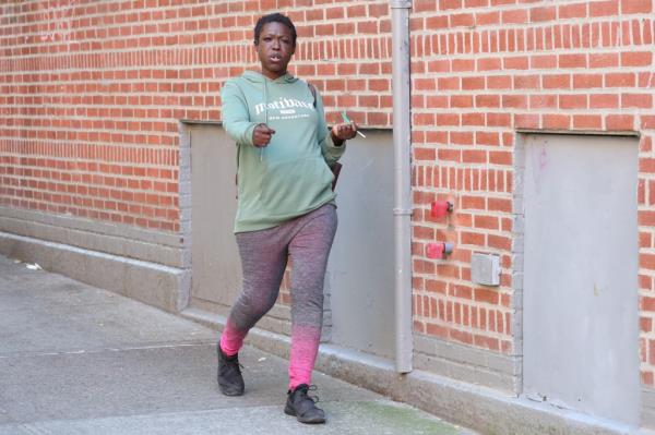 Female perp in green sweater walking in front of the store wher<em></em>e she committed the crime