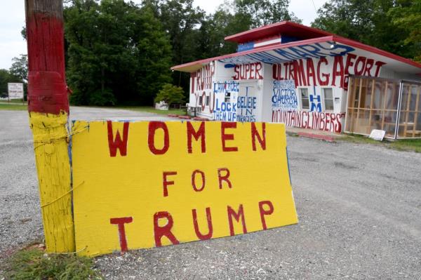 Man standing among various signs supporting Do<em></em>nald Trump and Moms for Liberty, and against Communism on his rural property filled with junked vehicles and American flags in Fountain, Michigan