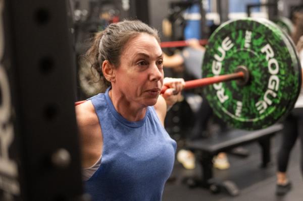 Allison Webber seen with barbell on pack as she squats during a group strength training class at The Training Lab.