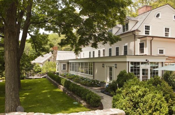 Exterior view of the luxurious Bedford Post Inn co-owned by Richard Gere and Russell Hernandez, featuring a large house surrounded by a lawn and trees.