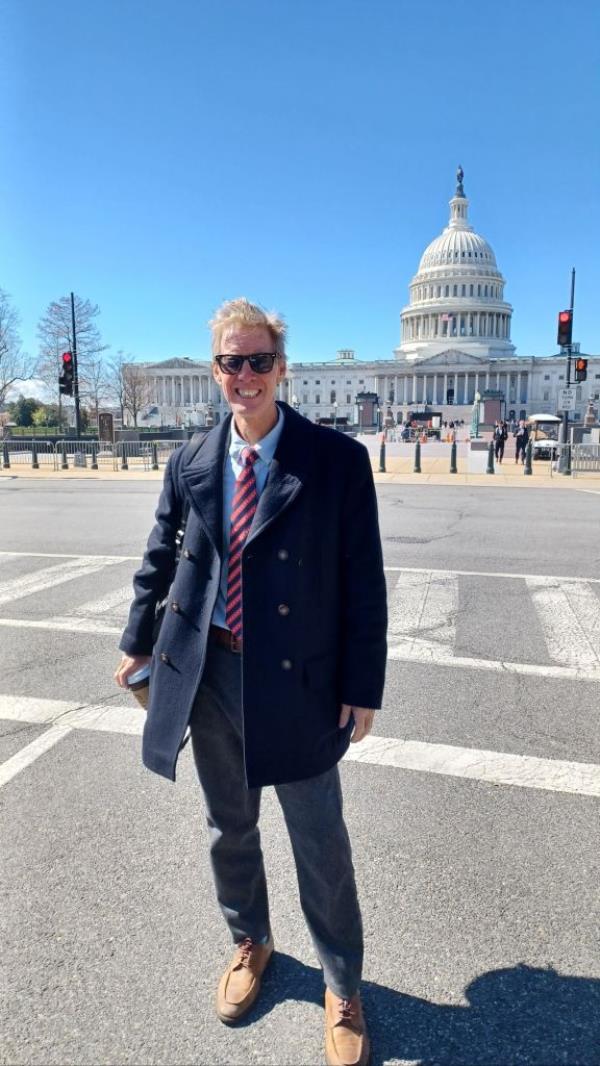Ryan Wesley Routh, 58, in a suit and tie standing in front of a white house after being taken into custody, with his tweet a<em></em>bout DEMOCRACY being on the ballot.