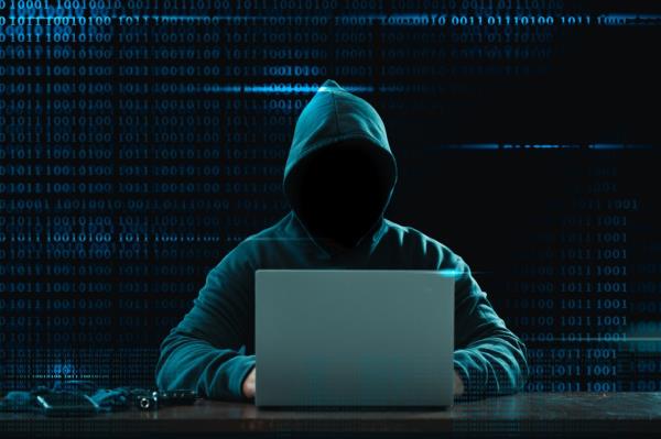 An ano<em></em>nymous hacker in a hoodie hacking into protected financial data on a laptop