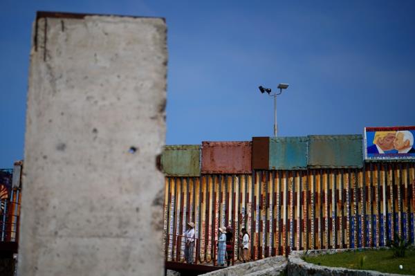 People walk along the wall that separates the United States from Mexico, near a slab of the Berlin Wall, in Tijuana, Mexico, Friday, Aug. 25, 2023.