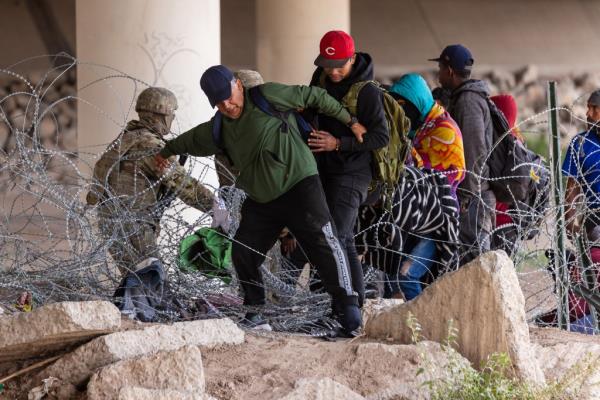 Migrants attempt to cross barbed wire into the US.