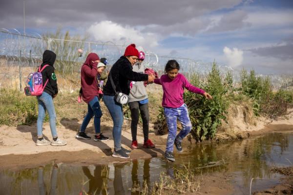 migrants by the Rio Grande, which is shallow, wire and fencing in the background.