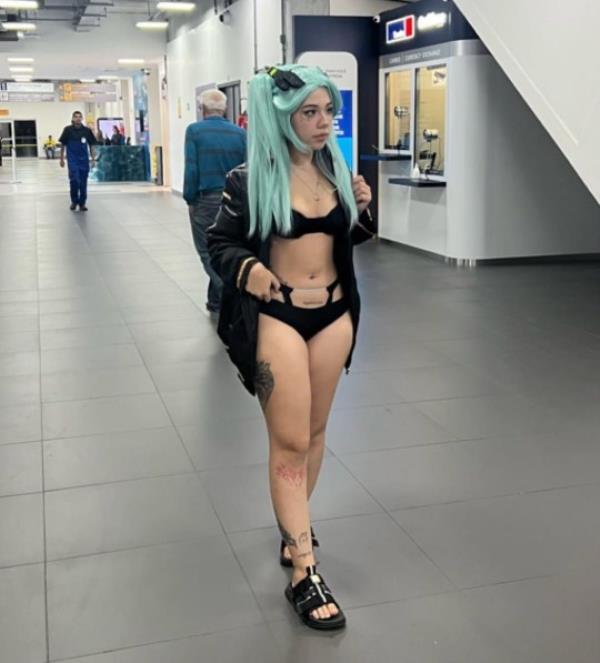 Story from Jam Press (Cosplay Flight Ban) Pictured: Kine-Chan at the airport. 'I was banned from boarding my flight and told to go home and change clothes' A woman claims to have been banned from boarding a flight after dressing in cosplay at the airport. Kine-Chan, a 21-year-old model, influencer and o<em></em>nlyFans co<em></em>ntent creator, appeared at Navegantes Airport in Brazil, dressed in ?Rebecca's Cosplay?. Wearing o<em></em>nly a black bikini, turquoise wig and black sandals, she claims she was told she wasn?t dressed appropriately and was banned from boarding the flight. Sharing the alleged incident on Instagram (@kinechan2.0) with her 612,000 followers, Kine-Chan wrote: ?Xuxus, a very annoying situation happened this weekend!? ?I tried to board at Navegantes airport dressed as Rebecca's Cosplay for an event. ?I already knew that I could be late, so I was dressed so as not to waste time and could go straight to my room. ?But I was told to go home and change clothes because the one I was wearing was not ?appropriate?. ?I explained that I was going to an event. ?Anyway Rebecca barred lol.? Dressed as the fictio<em></em>nal character Rebecca from the anime series Cyberpink: Edgerunners, Kine-Chan do<em></em>nned the skimpy outfit before being allegedly stopped by airport security and barred from co<em></em>ntinuing to her flight. Fans have rushed to comment on her antics, many thinking she has gone too far. ?Kine i love you but for the love of God... you could have put on an easy pull-up outfit, like a falling dress or even a button-down blouse,? commented Jazz. [sic] Bruno added: ?THEY WERE RIGHT, YOU COULD HAVE PUT THAT CLOTHES ON THERE, THEY WERE SURE, NOT GOING TO LET YOU BOARD.? [sic] Page wrote: ?AMG, it didn?t hurt to wear a dressing gown on top.? [sic] ?Man I work shows and my schedule in between shows is pretty short... I'm going with my costume and ON TOP I'll put a robe or an overalls! Here's the tip for you,? said Leticia. [sic] Jam Pres